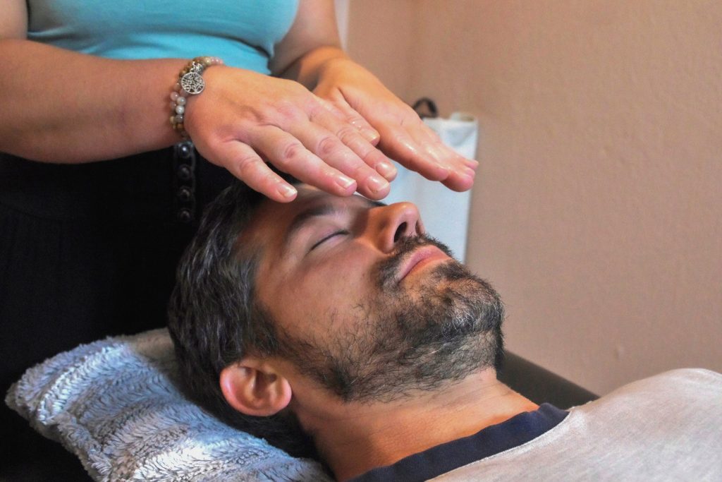 Soin Reiki Tao Tö Qi : les mains de Laëtitia Campi posées sur le front d'un homme allongé, au cabinet
